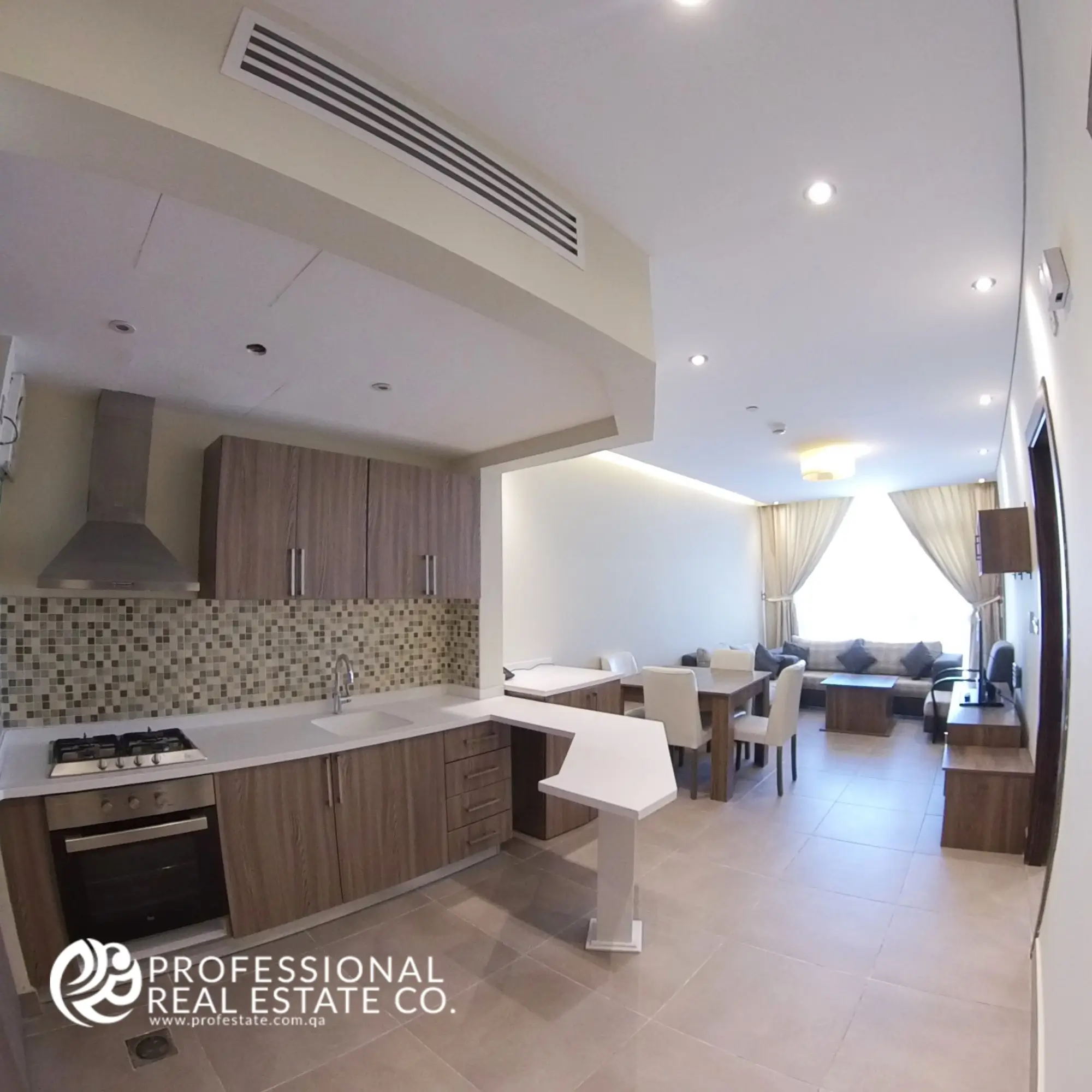 View of the open kitchen and living room in the fully furnished 1-bedroom apartment in Al Sadd, Doha, showcasing a modern design with seamless integration of living and dining spaces, ideal for comfort and entertaining.