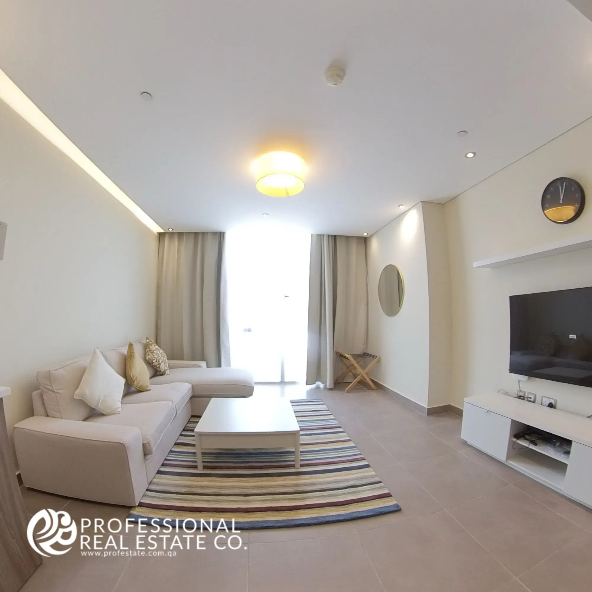 Alternative view showcasing the window side of the living room in a fully furnished 2 BHK apartment in Al Sadd, with abundant natural light and spacious design.
