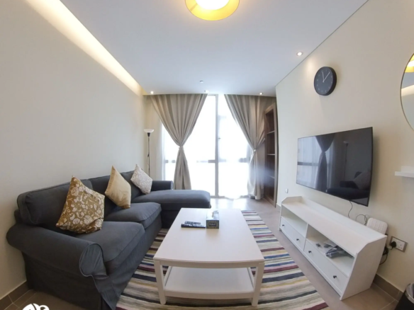 Alternative view of the living room showcasing the window side in a fully furnished 1 BHK apartment in Al Sadd, emphasizing natural light and open space.