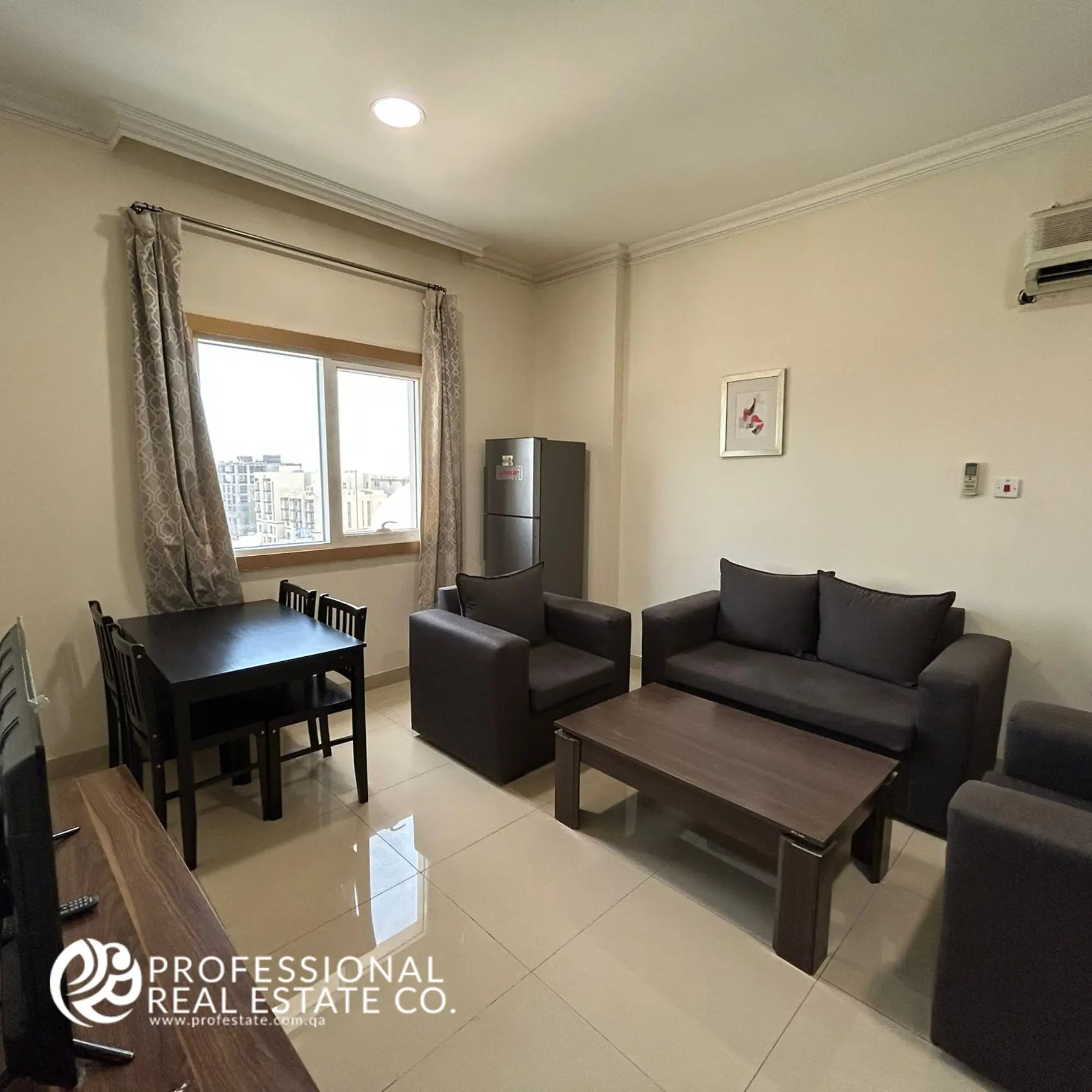 Living and dining area with window view in a fully furnished 1 BHK apartment in Umm Ghwailina, featuring natural light, cozy seating, and a compact dining setup.