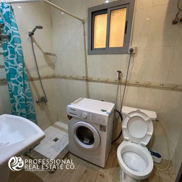 Compact toilet room with shower in a fully furnished 1 BHK apartment in Umm Ghwailina, featuring a space-efficient design and modern fixtures.