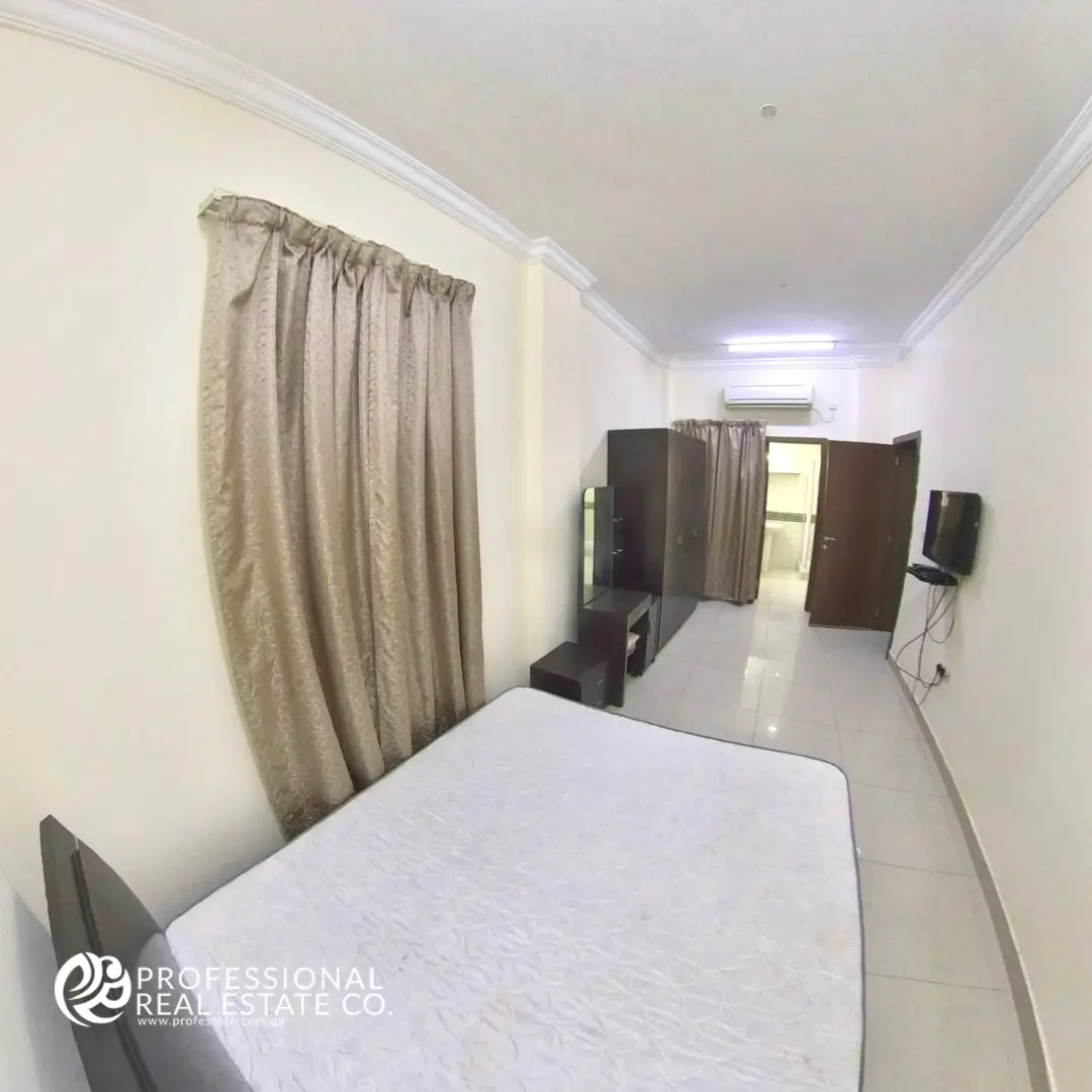 Bedroom area with bed facing toilet room in fully furnished studio apartment in Bin Mahmoud, Doha